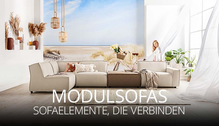 Helles Wohnzimmer mit beigen Modulsofas, dekorativen Kissen und Decken, Pflanzen und leichter Brise durch offene Fenster, entspannte Atmosphäre mit Strandmotiv im Hintergrund.