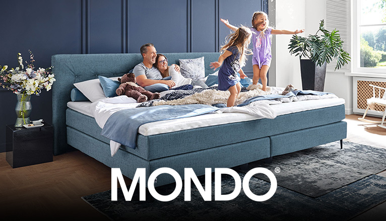 MONDO Schlafen bei Moebel-Shop - Eine Familie mit zwei Kindern in einem blauen MONDO Familien-Boxspringbett. Die Eltern liegen Arm in Arm und schauen lachend zu, wie ihre Kinder auf dem Bett freudestrahlend hüpfen.