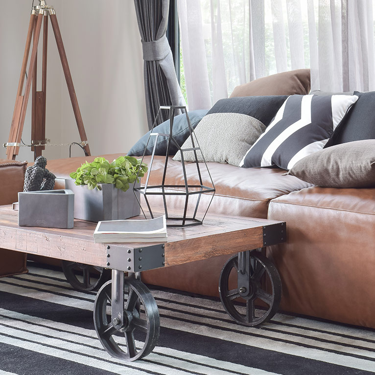 Wohnzimmer im Loft-Stil mit Ledersofa, Couchtisch auf Rollen, industriellen Metallelementen, dekorativen Wohnaccessoires und modernen Schwarz-Weiß-Akzenten.