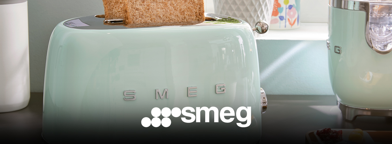 smeg Toaster bei Moebel-Shop – Mintgrüner Toaster mit 2 Toasts und ein Standmixer auf holzfarbener Arbeitsplatte vor einem Fenster, daneben steht ein Kuchenteller – farblich perfekt abgestimmt.
