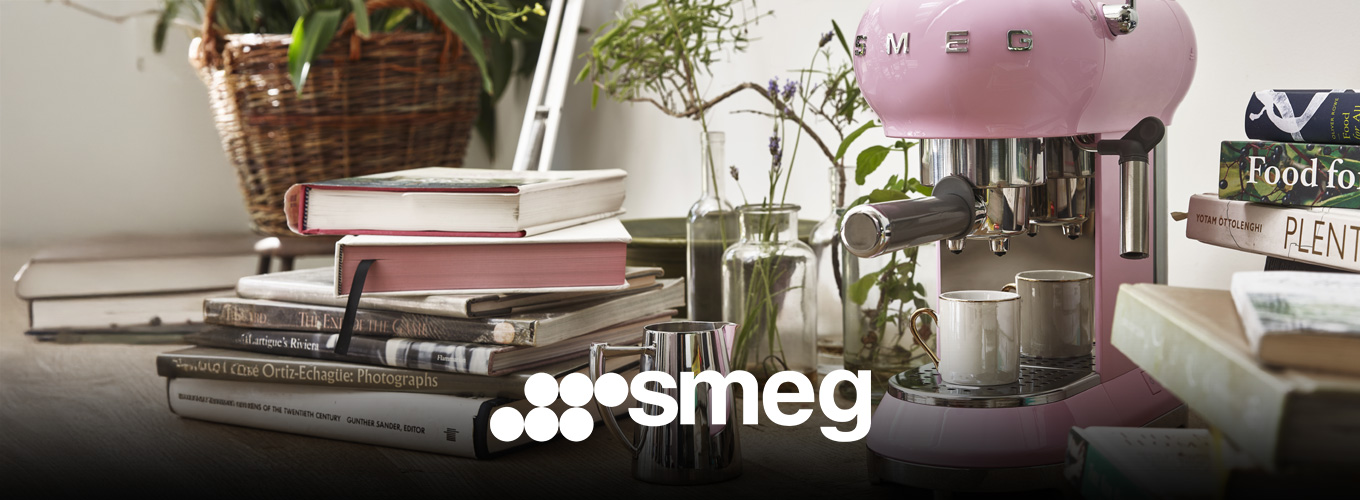 smeg Kaffeemaschinen bei Moebel-Shop – Rosa SMEG Espressomaschine mit Edelstahl-Milchkännchen daneben auf einer Arbeitsplatte mit Bücherstapeln daneben