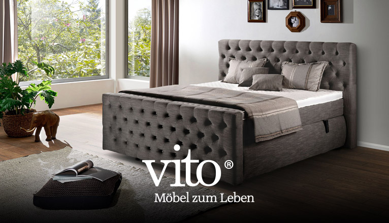 vito Schlafen bei Moebel-Shop - Ein glänzend taupefarbenes vito Boxspringbett in einem Schlafzimmer mit großen Fenstern und passenden Vorhängen