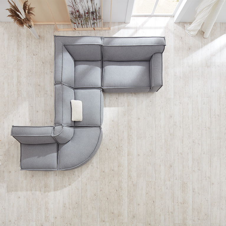 Modulares, hellgraues Sofa mit runder Ecke und einem Zierkissen, aus der Vogelperspektive aufgenommen, auf hellem Holzfußboden in einem modern eingerichteten Raum.