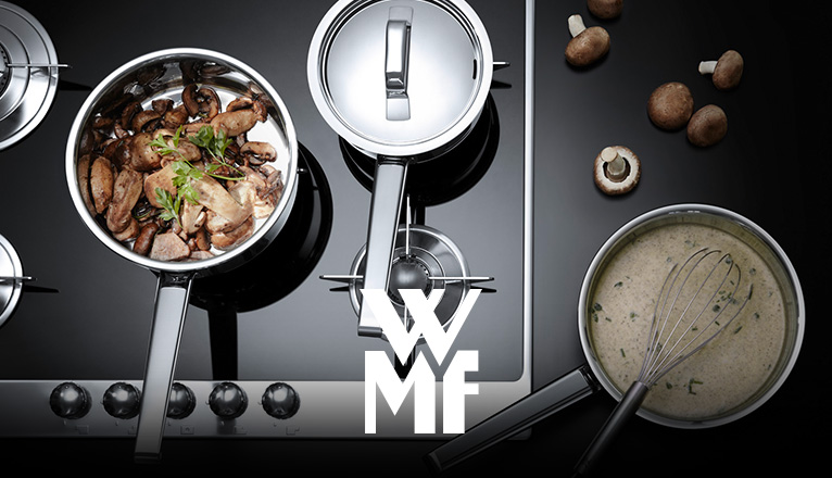 WMF bei Moebel-Shop - Blick von oben auf einen Herd mit mehreren WMF-Töpfen und Pfannen, in denen Essen zubereitet wird; in einem Topf steckt ein Schneebesen.