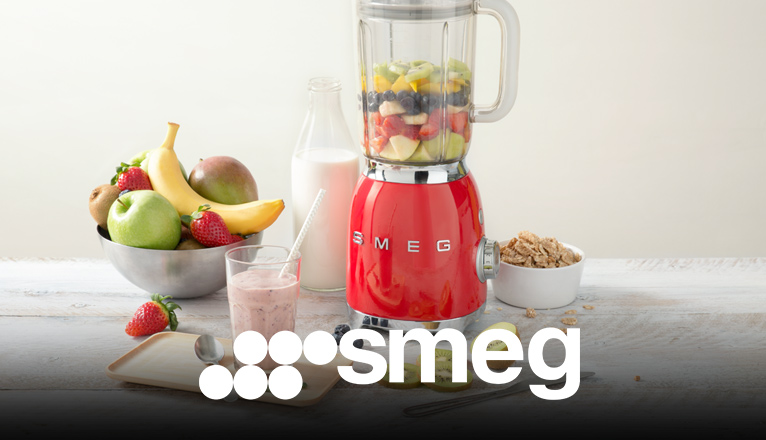smeg Standmixer bei Moebel-Shop – Roter SMEG Standmixer mit einem gemixten Smoothie in einem Glas mit Strohhalm, eine Schale mit Obst, eine Flasche Milch und eine Schale mit Cerealien stehen daneben