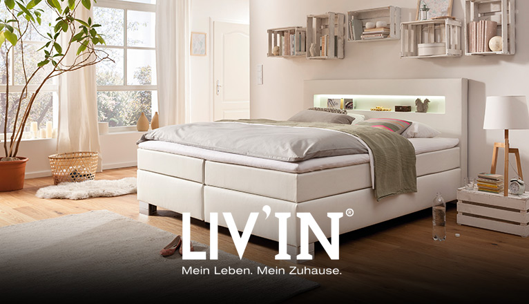 LIV’IN Schlafen bei Moebel-Shop - Weißes Boxspringbett mit beleuchtetem Kopfteil. Rustikale Wandregale aus Holzkisten ergänzen das gemütlich eingerichtete Schlafzimmer mit Holzfußboden.