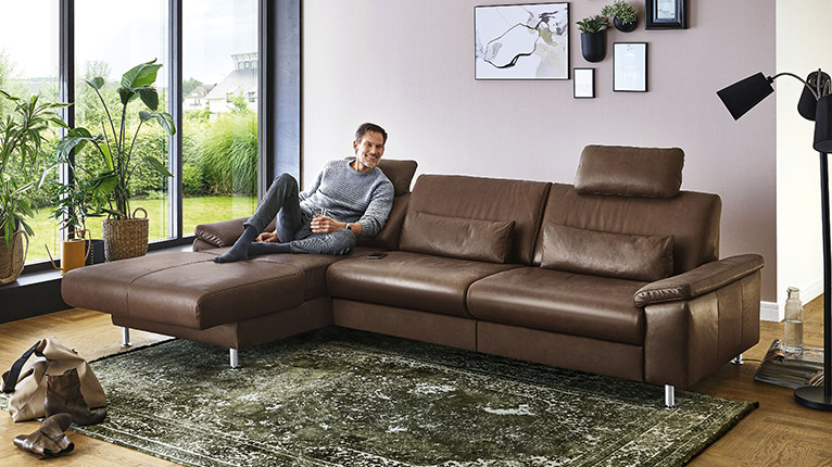vito Sofas bei Moebel-Shop - Ein Mann sitzt entspannt auf einem braunen vito Ledersofa mit einem Glas Wasser in der Hand