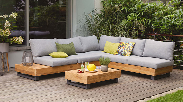outdoor Lounge-Gruppen bei Moebel-Shop - Eine outdoor Lounge-Ecke mit Alufuß und Holz, dazu passender outdoor Lounge-Tisch auf Terrasse, Grünpflanzen und halbe Fensterfront im Hintergrund