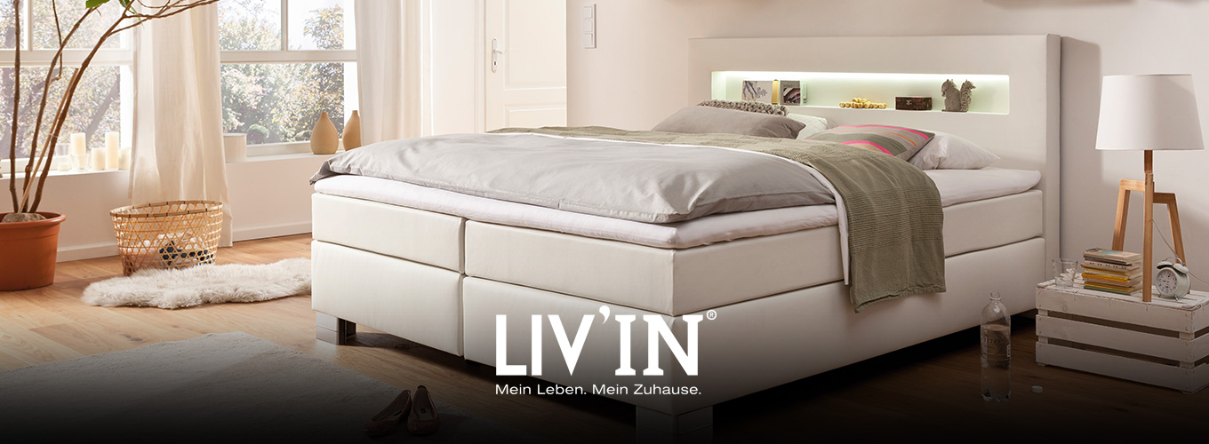 LIV’IN Schlafen bei Moebel-Shop - Weißes Boxspringbett mit beleuchtetem Kopfteil. Rustikale Wandregale aus Holzkisten ergänzen das gemütlich eingerichtete Schlafzimmer mit Holzfußboden.