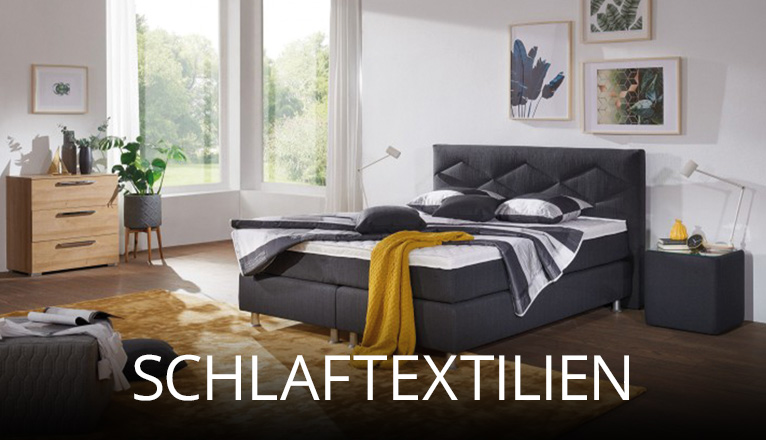 Gemütliches Schlafzimmer mit grauem Boxspringbett, dekorativen Kissen und Decken in kontrastreichen Farben, ergänzt durch Teppich, Kommode und große Fenster, die für viel Tageslicht sorgen