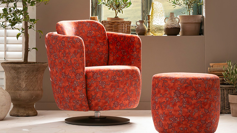 Jetzt Bassetti Sessel entdecken! - Ein orange-roter Bassetti Polstersessel steht in einem italienischen Ambiente, vor einem Fenster, das einen Blick in eine toskanische Landschaft zulässt. Kleine Olivenbäume dekorieren den Raum.