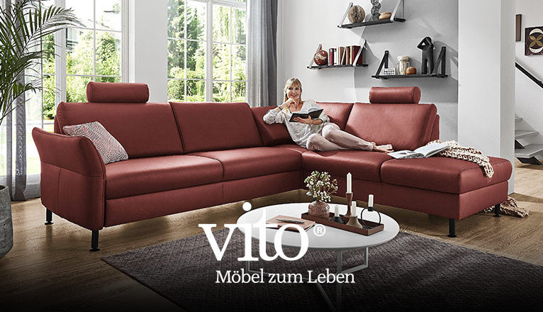 vito - Möbel zum Leben - bei Moebel-Shop - Eine Frau sitzt in einem Wohnzimmer in gemütlicher Position auf einem roten vito Ledersofa und hält ein Buch in den Händen