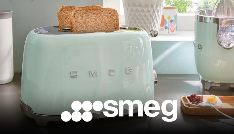 smeg Toaster bei Moebel-Shop – Mintgrüner Toaster mit 2 Toasts und ein Standmixer auf holzfarbener Arbeitsplatte vor einem Fenster, daneben steht ein Kuchenteller – farblich perfekt abgestimmt.