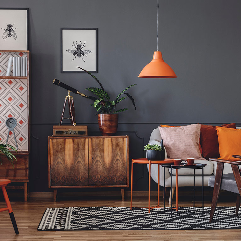 Wohnzimmer im Retro-Stil mit Mid-Century-Möbeln, Holzkommode, orangefarbenen Akzenten, dekorativen Wohnaccessoires und grafischem Teppich für nostalgisches Flair.