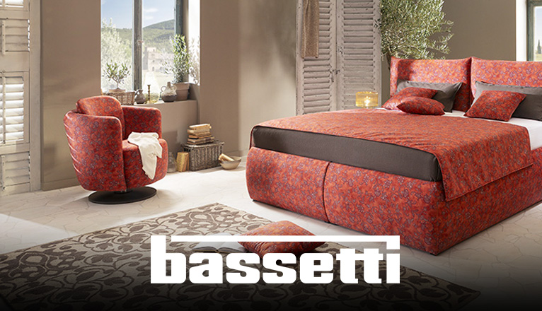 Jetzt Bassetti Sessel entdecken! - Ein orange-roter Bassetti Polstersessel steht in einem italienischen Ambiente, vor einem Fenster, das einen Blick in eine toskanische Landschaft zulässt. Kleine Olivenbäume dekorieren den Raum.
