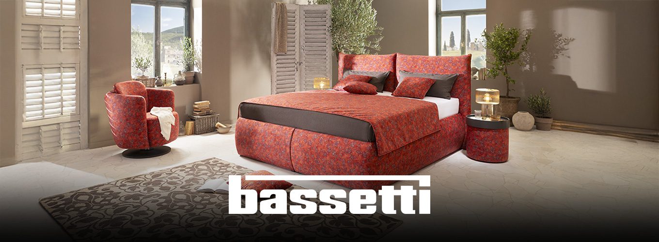 Jetzt Bassetti Sessel entdecken! - Ein orange-roter Bassetti Polstersessel steht in einem italienischen Ambiente, vor einem Fenster, das einen Blick in eine toskanische Landschaft zulässt. Kleine Olivenbäume dekorieren den Raum.
