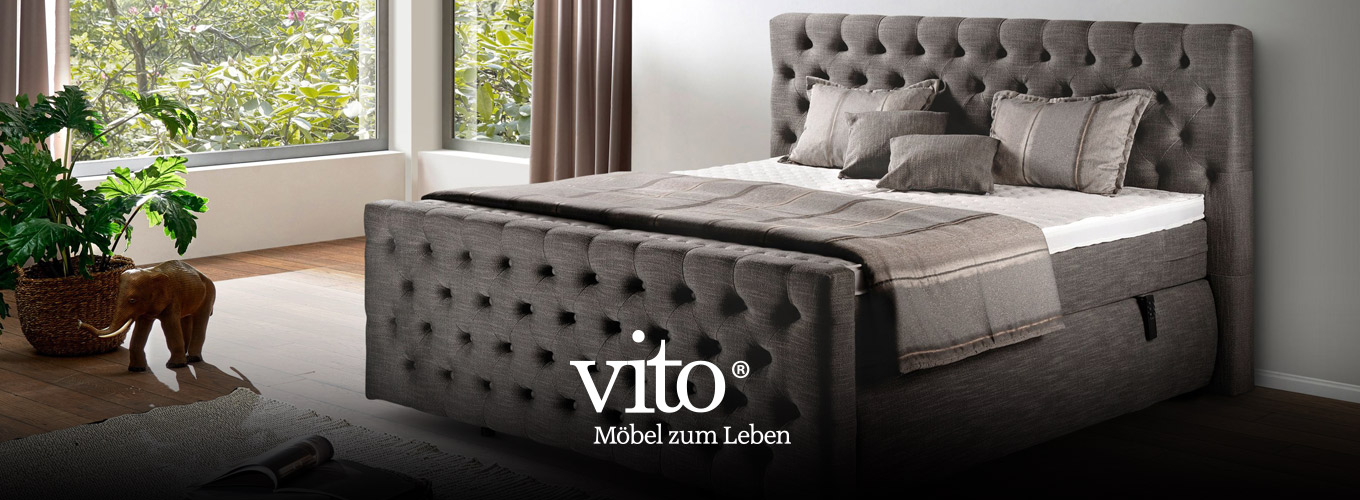 vito Schlafen bei Moebel-Shop - Ein glänzend taupefarbenes vito Boxspringbett in einem Schlafzimmer mit großen Fenstern und passenden Vorhängen