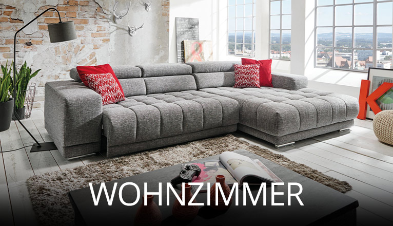 Helles Wohnzimmer mit großer grauer Eckcouch, roten Kissen als Farbakzent, dekorativen Elementen und Pflanzen, kombiniert mit loftartiger Backsteinwand und Panoramafenstern für urbanes Flair