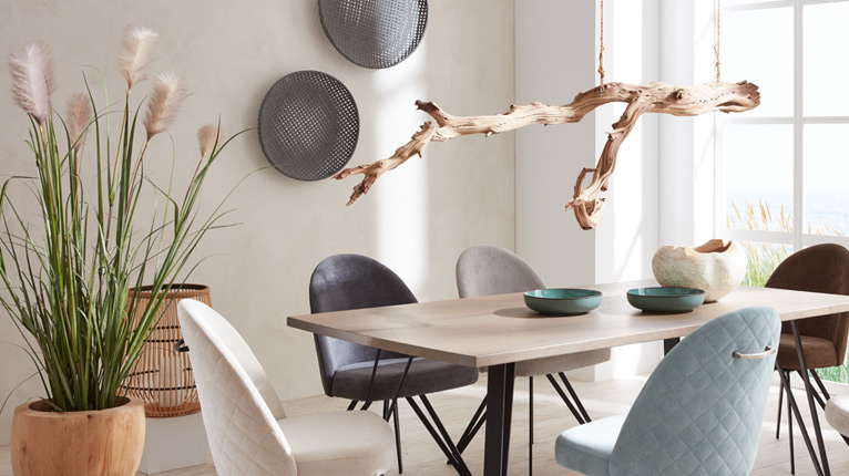SANSIBAR LIVING Dekoration bei Moebel-Shop - Ein Esstisch mit unterschiedlichen Polsterstühlen in Creme, Grau und Taupetönen, mintfarbene Schüsseln stehen auf dem Tisch, Wanddeko und schwebender Deko-Ast über dem Tisch