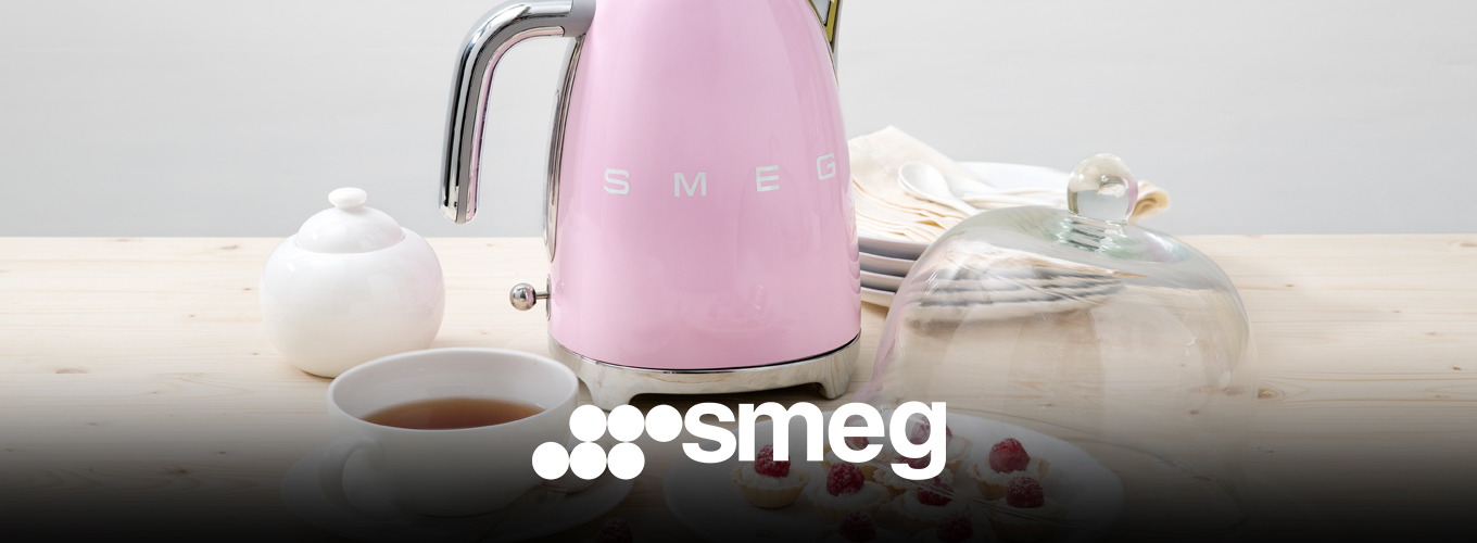 smeg Wasserkocher bei Moebel-Shop – Rosa SMEG Wasserkocher mit Teetasse, Zuckerdose und passenden, weißen Tellern. Auf dem Teller im Vordergrund liegen kleine Himbeertörtchen eine Glasabdeckung liegt halb darauf