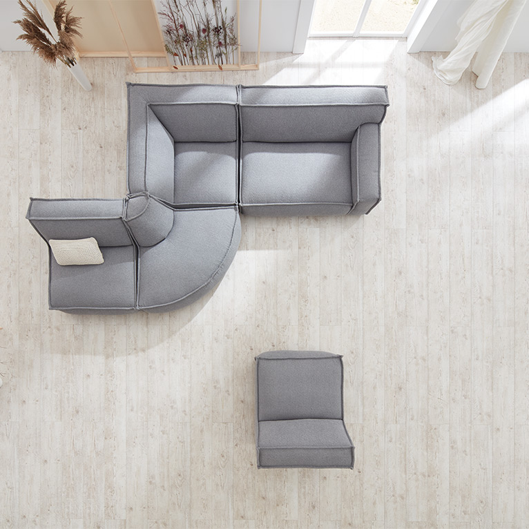 Hellgraues, modulares Sofa mit abgerundeter Ecke und separatem Einzelsitz, von oben aufgenommen auf hellem Holzfußboden in modernem, lichtdurchflutetem Wohnambiente.